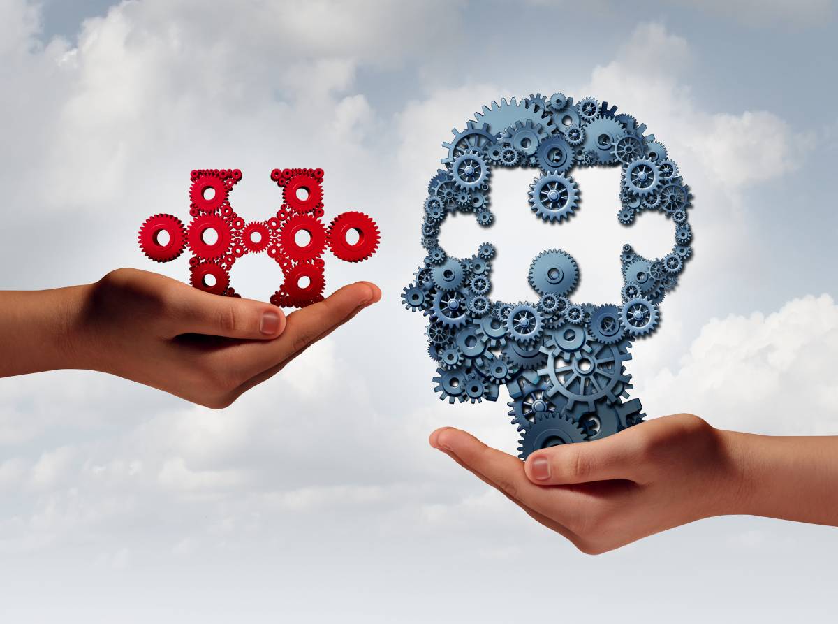 Two hands out-stretched, one on the left and another on the right, holding things made up of gears, one in the shape of a head a with a missing puzzle piece section and the other hand holding out the missing piece.