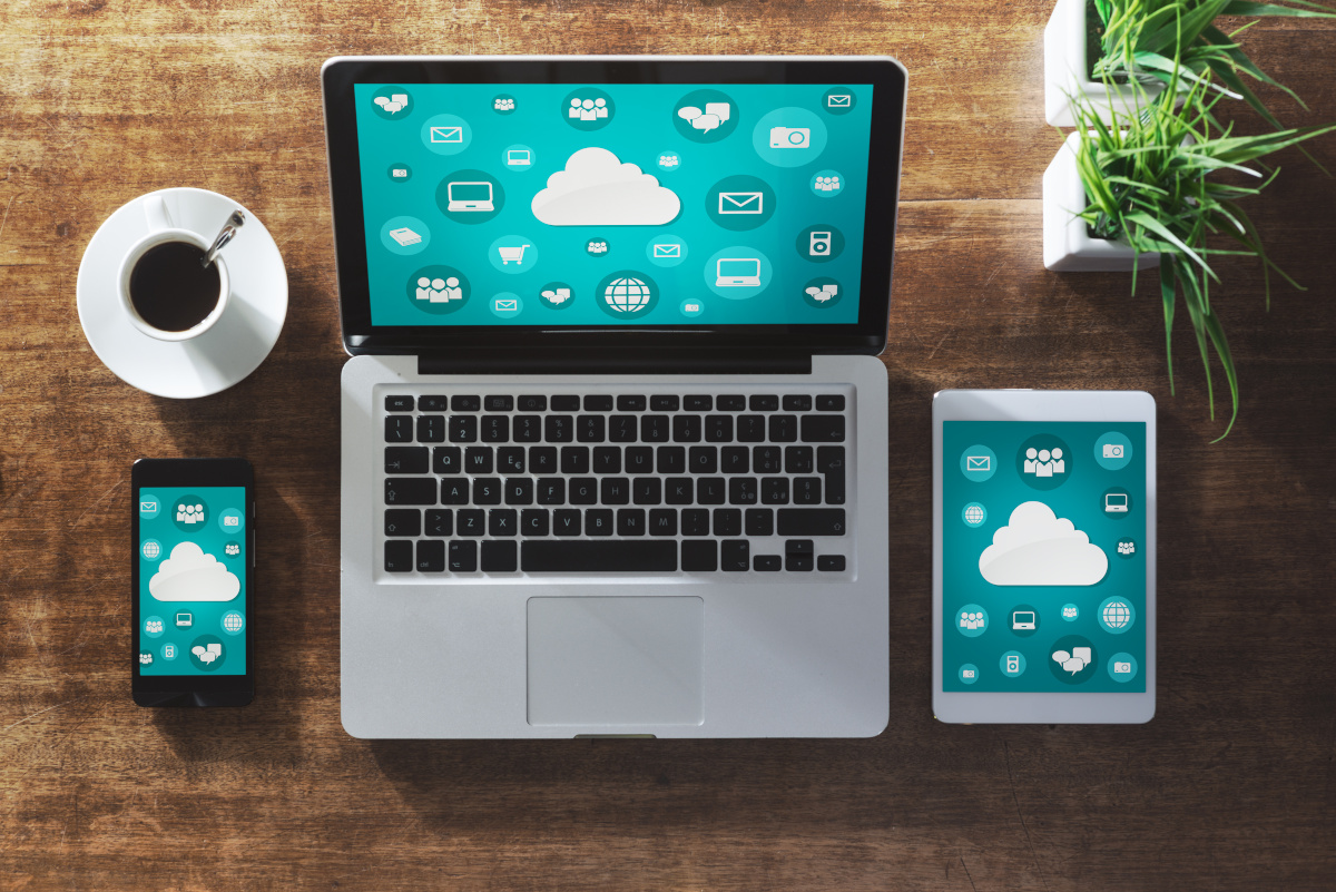 A smartphone, laptop, and tablet lined up on a desk, each displaying a cloud surrounded by multiple icons over greenish-blue background on their screens