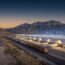 Distribution warehouse with loading docks and freight rail at dusk in Utah's Tooele Valley, with a network overlay